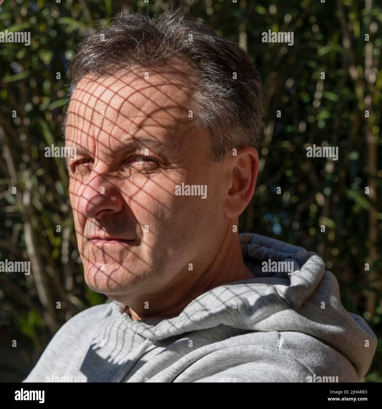 Porträt eines weißen Mannes mittleren Alters mit Schatten aus den Saiten eines Tennisschlägers über seinem Gesicht Stockfoto