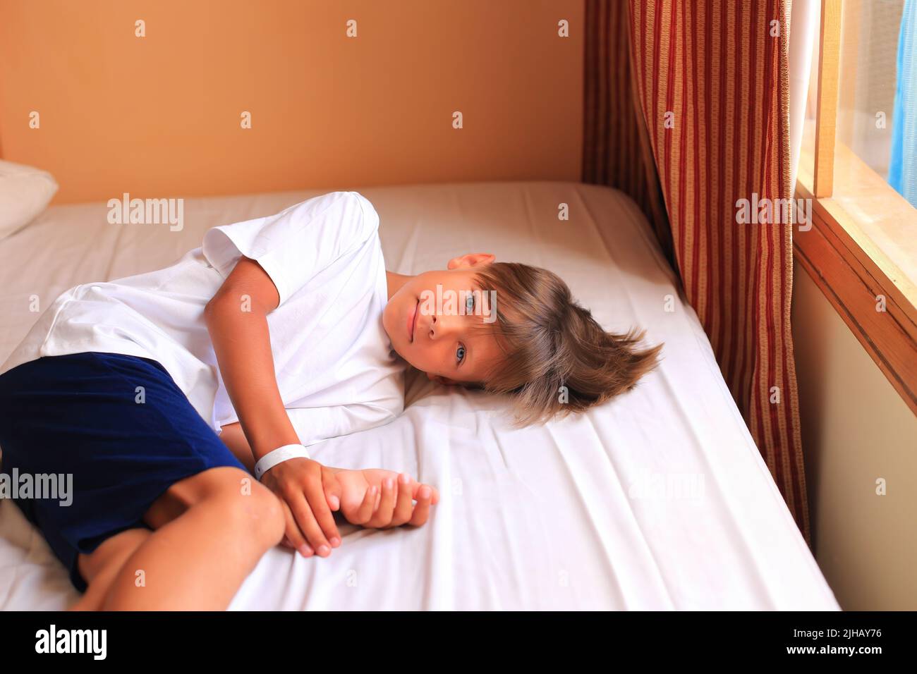 Ein Junge liegt in einem Hotelzimmer auf einem Bett mit weißen Laken. Das Kind schläft. Teenager auf dem Bett zu Hause Stockfoto