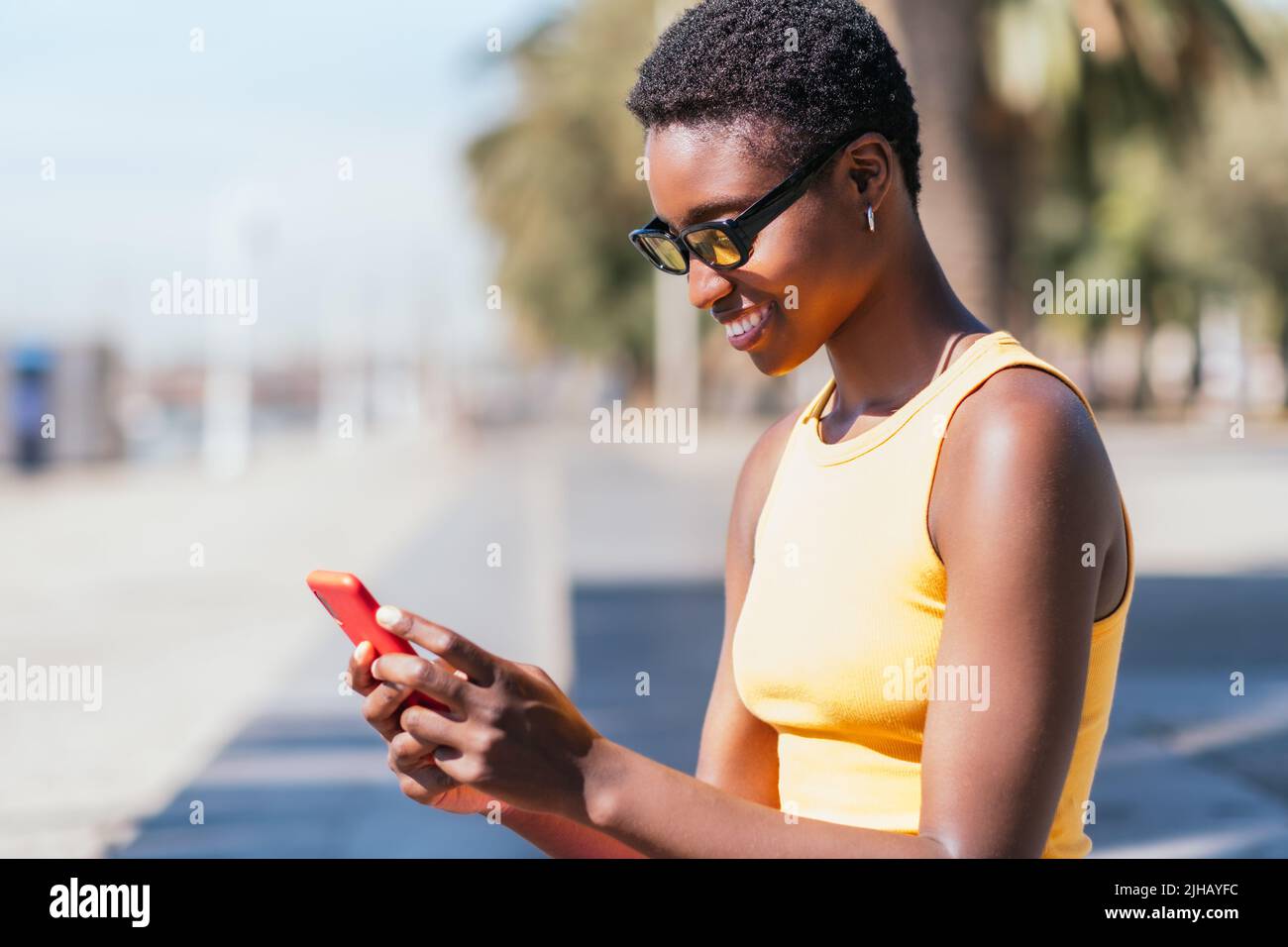 Trendige afroamerikanische Frau, die an einem sonnigen Sommertag ihr Telefon im Freien benutzt Stockfoto