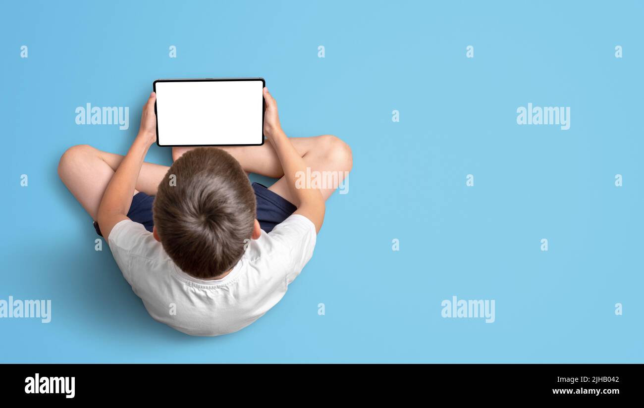 Boy hält ein Tablet. Isoliertes Display für Mockup, Website-Präsentation, App, Spiel. Blick von oben. Freier Speicherplatz für die Kopie auf blauem Hintergrund Stockfoto