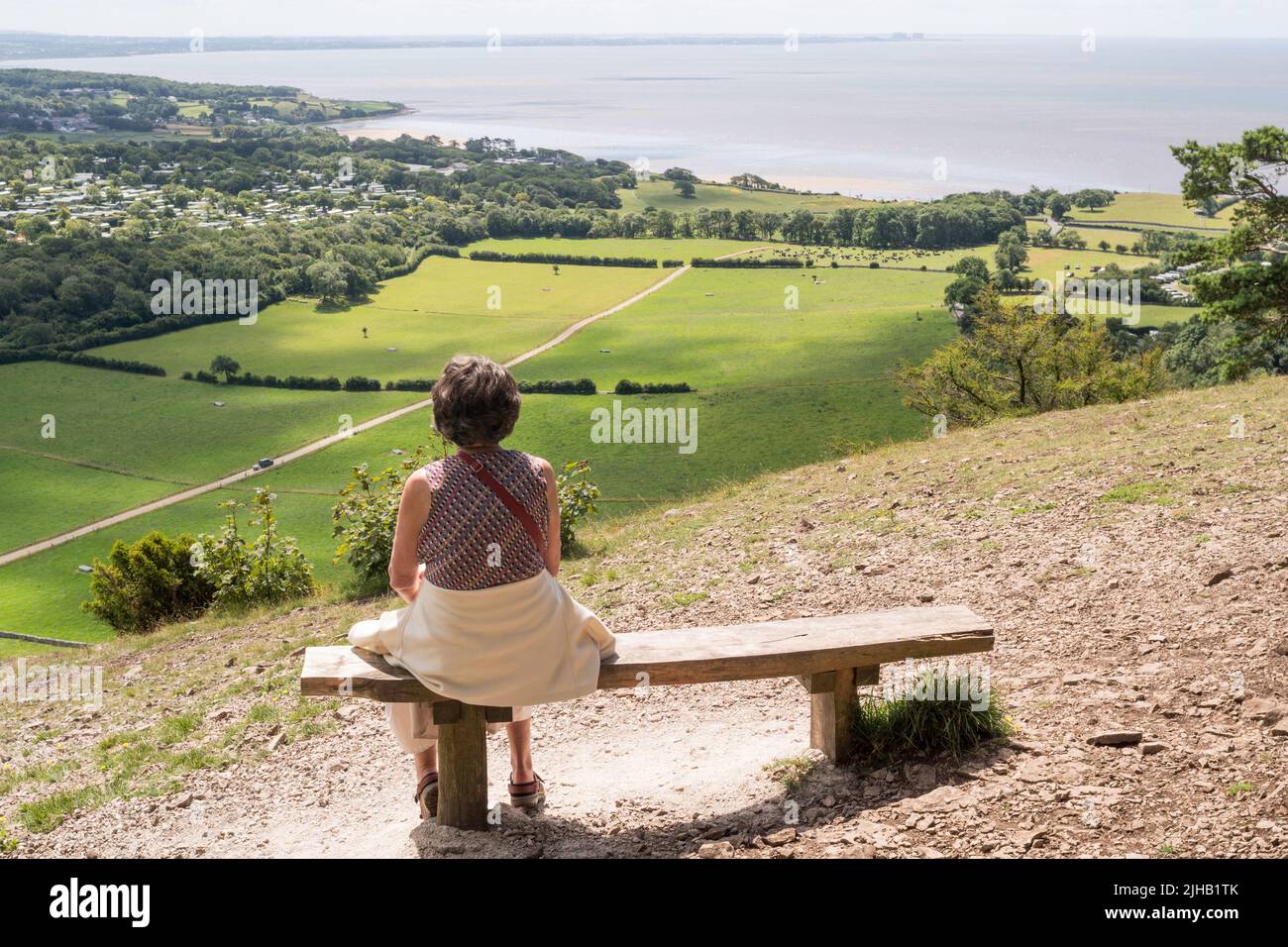 Eine Frau, die auf einer Bank über Arnside, Cumbria, England, Großbritannien, sitzt und die Morecambe Bay überblickt Stockfoto
