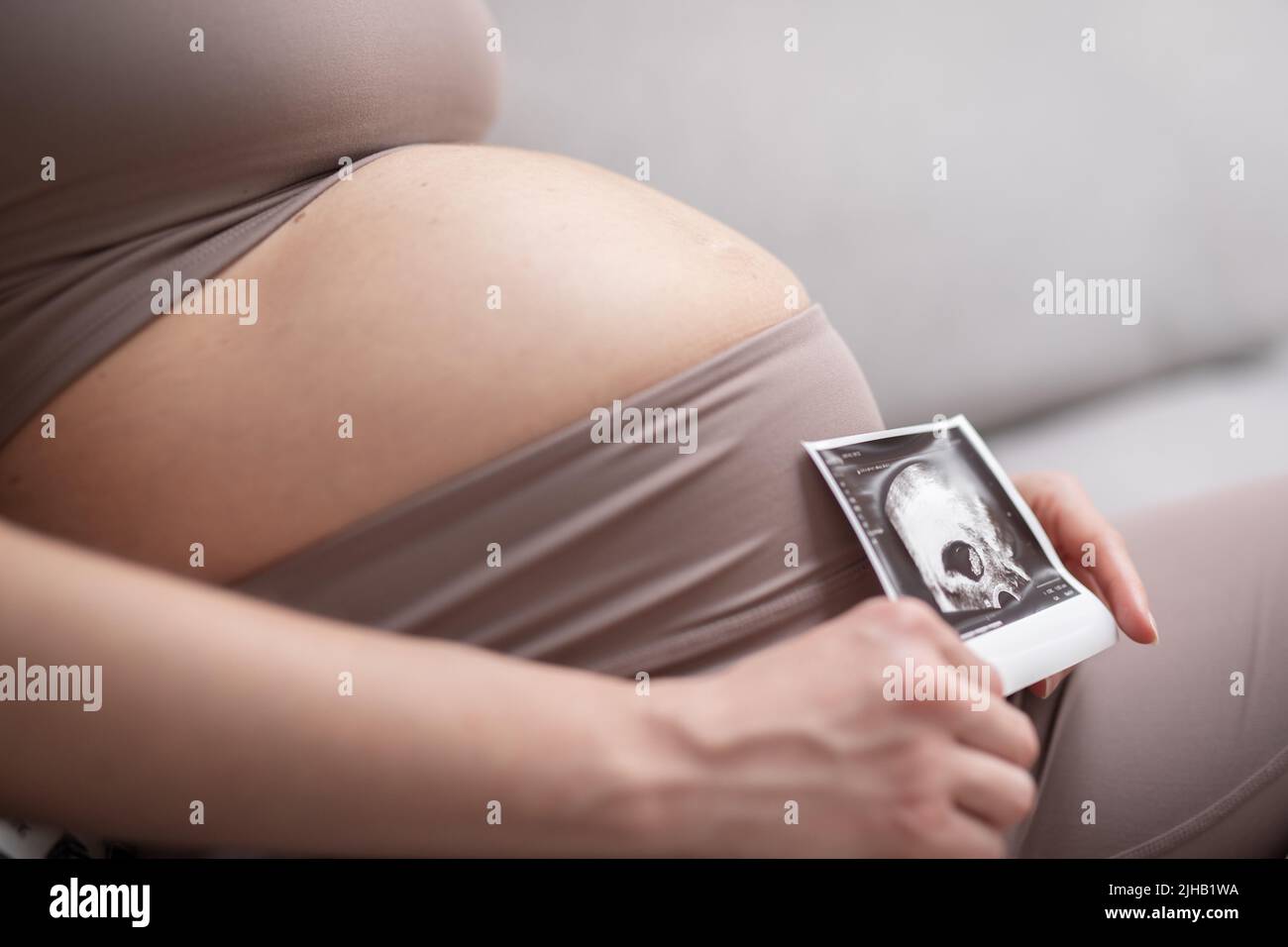 Bauch einer Schwangeren. Schwangerschaftskonzept. Schwanger Bauch Nahaufnahme. Detail der Schwangeren, die sich zu Hause auf dem bequemen Sofa entspannen. Stockfoto