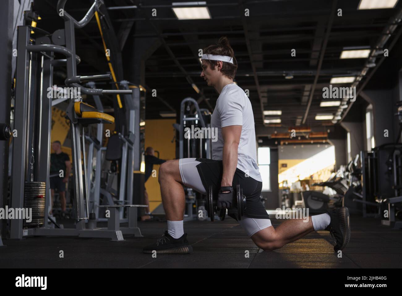 Ganzkörperaufnahme eines Fitnessmanns, der Ausfallschritte mit Kurzhanteln macht Stockfoto