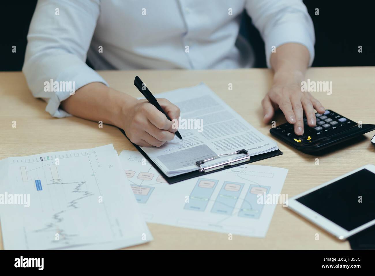 Nahaufnahme. Die Hände eines jungen Mannes ein Buchhalter in einem weißen Hemd, der an einem Schreibtisch mit Dokumenten, einem Taschenrechner, arbeitet, schreibt. Sitzen in einem modernen Büro Stockfoto