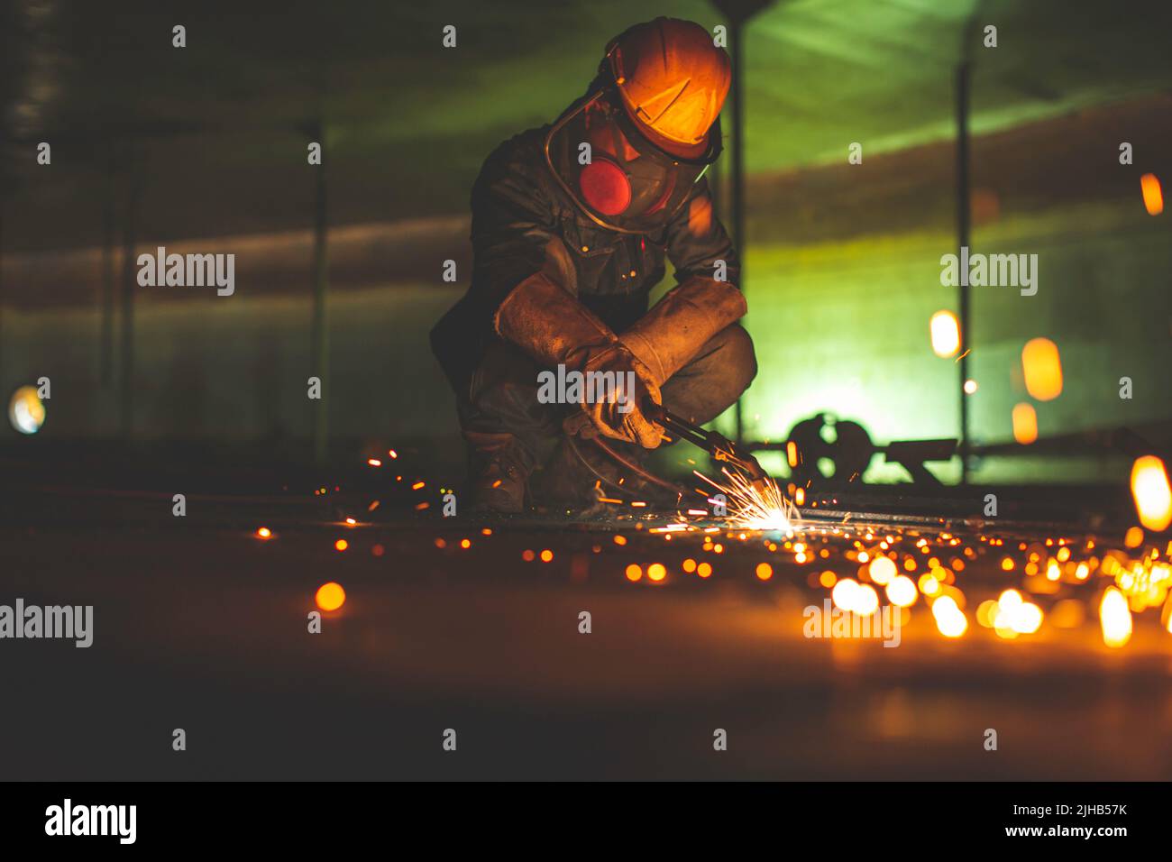 Metallspender des männlichen Arbeiters auf der Stahlplatte des Behälterbodens mit Blitzlicht in Nahaufnahme Schutzhandschuhe und Maske auf engem Raum tragen Stockfoto