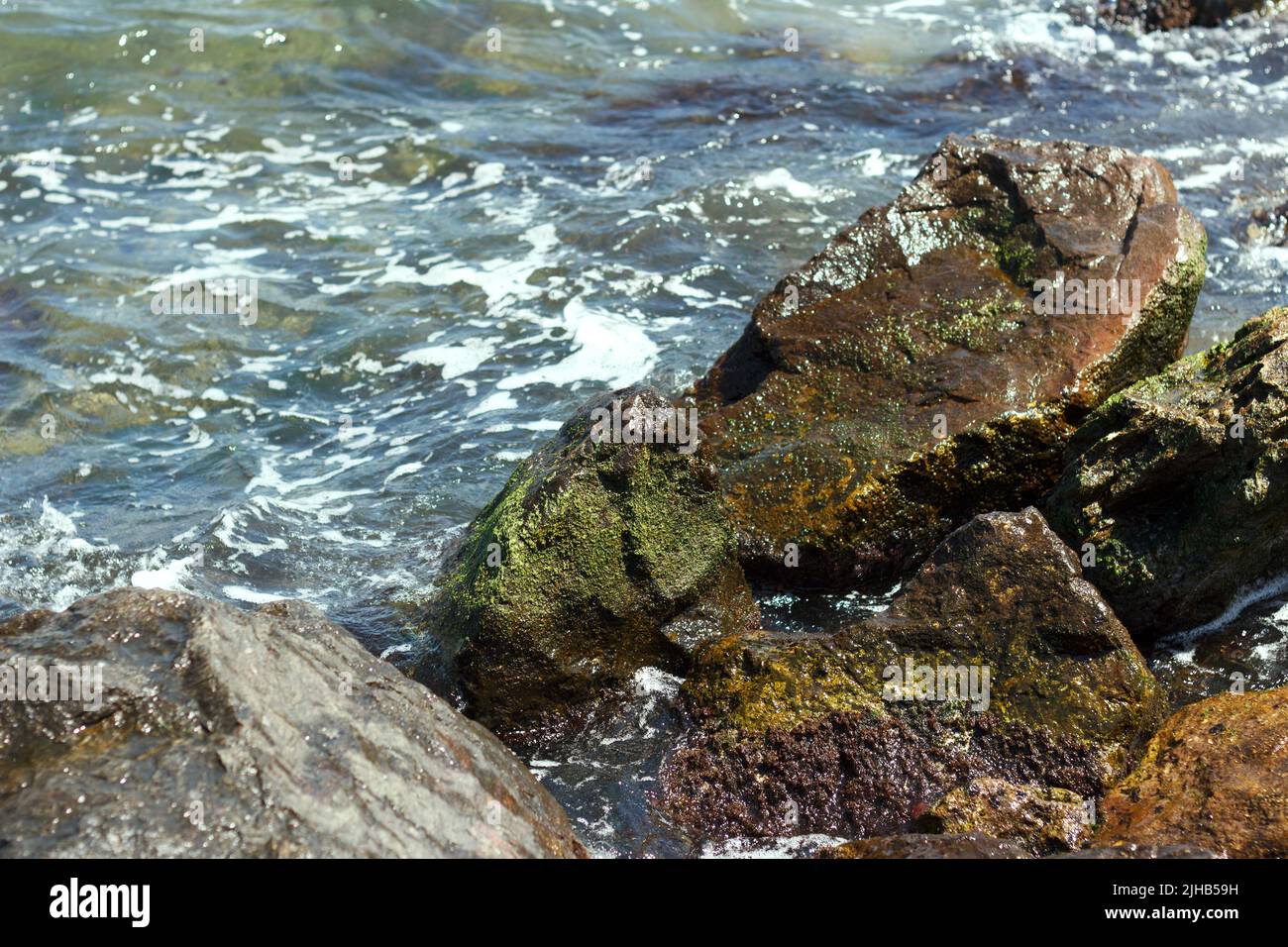 Die Meereswelle trifft auf die nassen Steine des Felsens Stockfoto