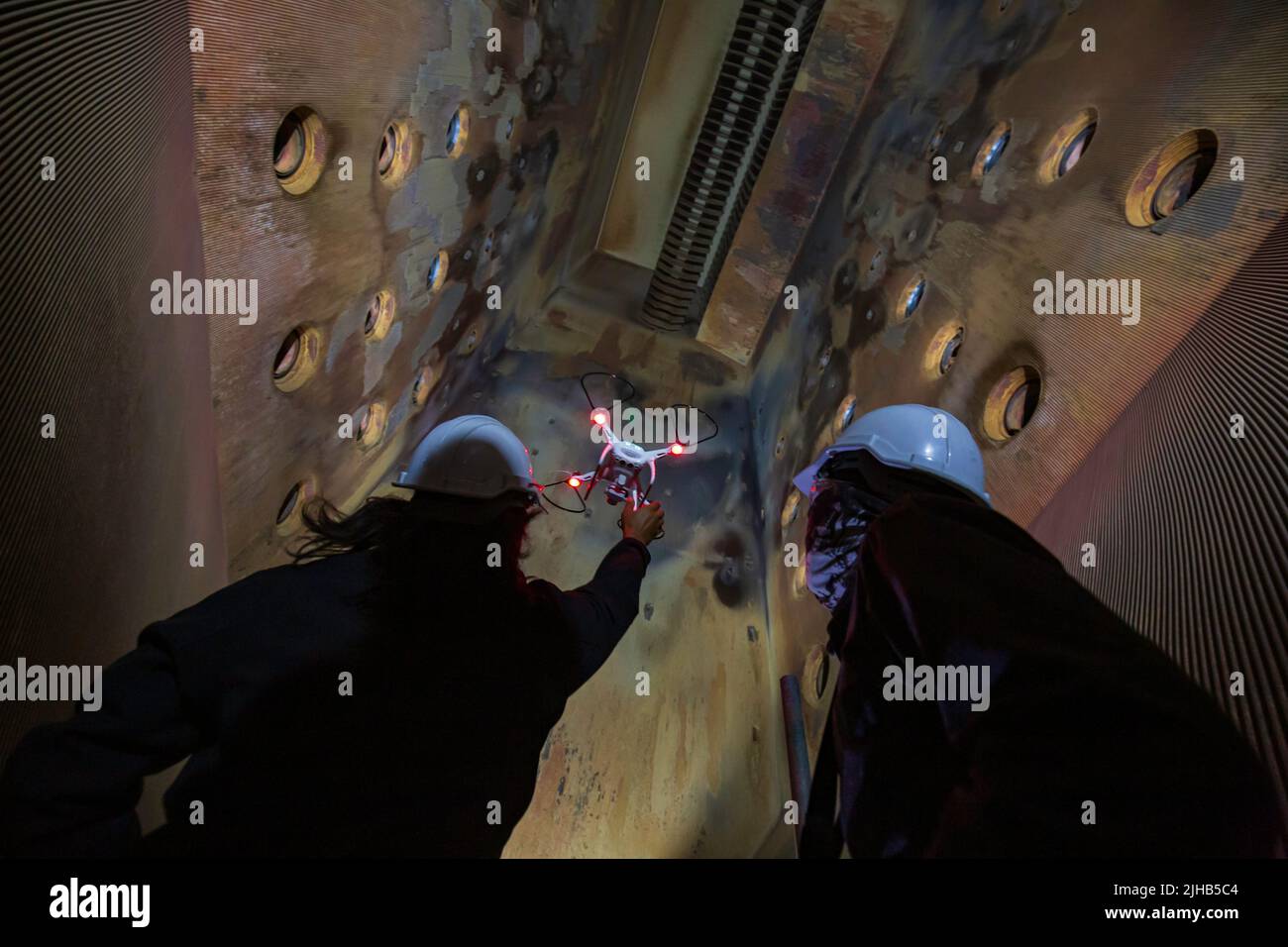 Inspektion von Drohnen-Männern durch Bauarbeiter am Ofen auf beengtem Gelände Stockfoto