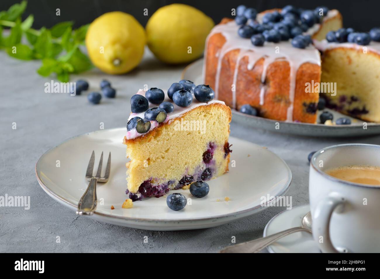 Zitronen-Blaubeerkuchen mit süßem Zuckerguss und Beeren überzogen, serviert mit Kaffee Stockfoto