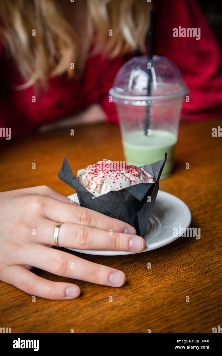 Eismatcha Latte und Cupcake aus der Nähe in einem Café in weiblicher Hand. Stockfoto