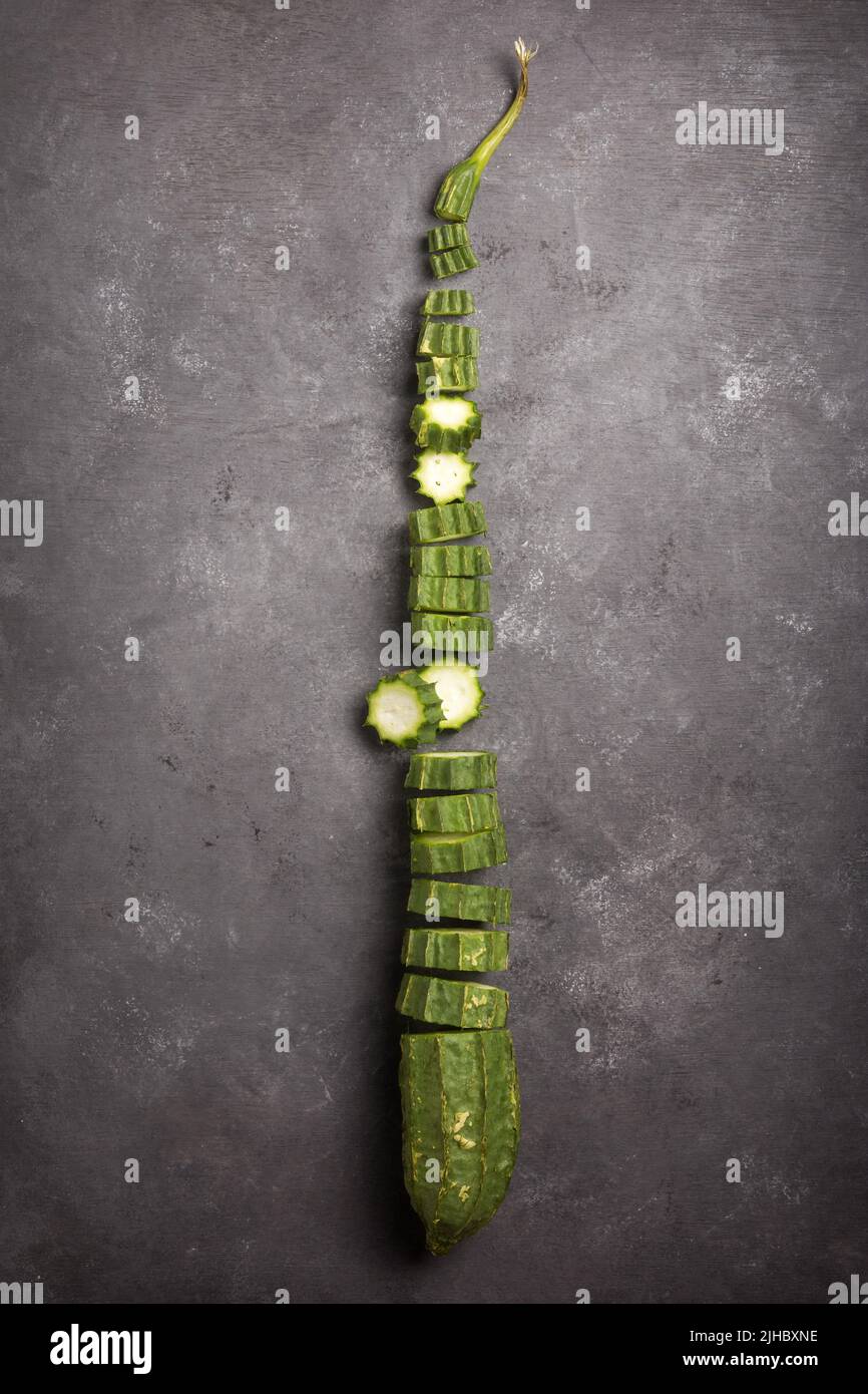 Frisch angewinkelte Luffa in Scheiben geschnitten auf einem schwarzen strukturierten Hintergrund, auch bekannt als gerippter Kürbis oder chinesische Okra, gesundes Gemüse von oben genommen Stockfoto