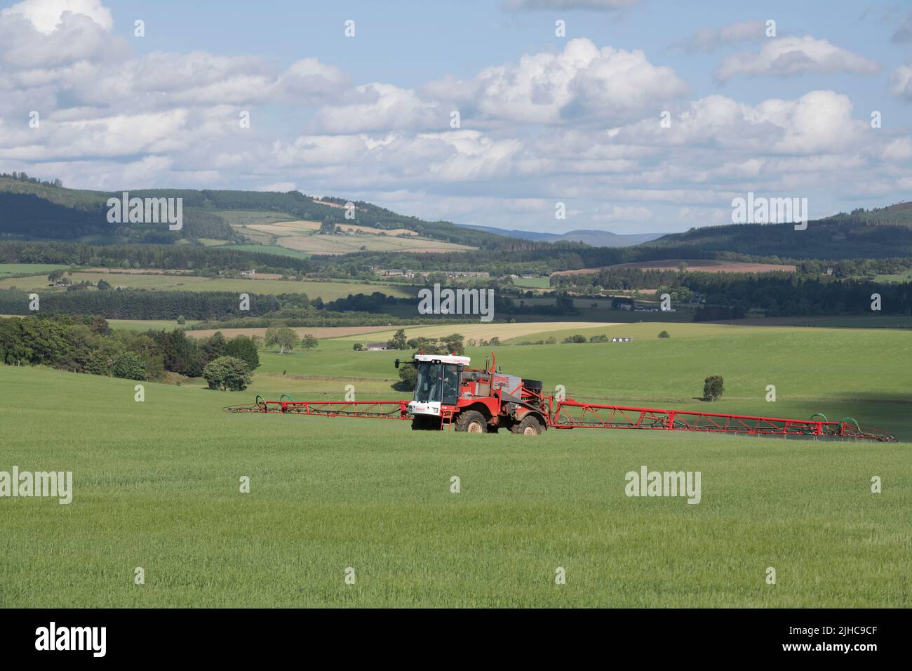 Eine Feldspritze, die an einem sonnigen Sommermorgen auf einem Feld mit landschaftlich reizvoller Aussicht auf die Landschaft von Aberdeenshire unterwegs ist. Stockfoto