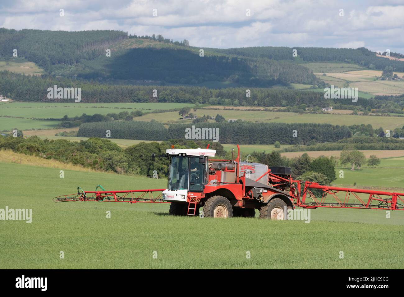 Ein Bateman-Sprüher, der Gerste auf einem Feld in Aberdeenshire sprühte und einen malerischen Blick auf die umliegende Landschaft bietet Stockfoto