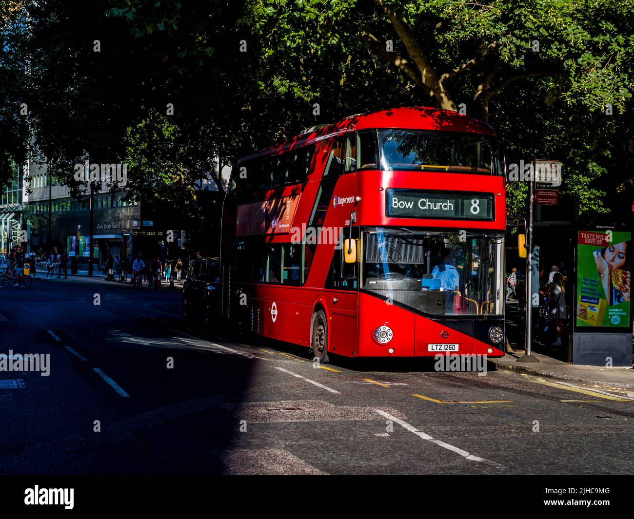 Der rote London Bus taucht im Zentrum Londons aus dem Schatten auf. Ein neuer Routemaster-Bus Nr. 8 zur Bow Church steht teilweise im Schatten in einer Londoner Straße. Stockfoto