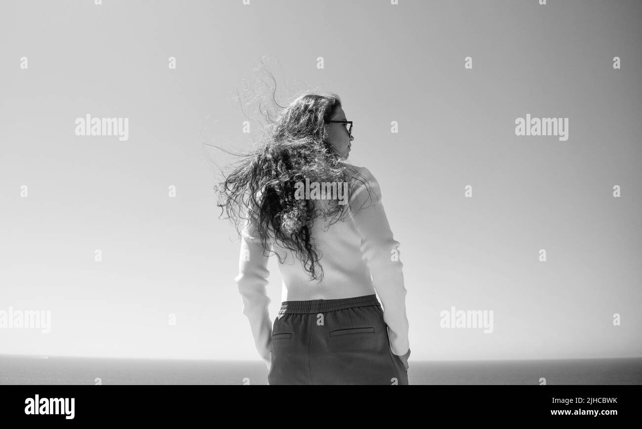 Ihr Haar fließt im Wind. Frau mit langen Haaren steht auf See. Stilvolle Mädchen mit welligen Frisur Stockfoto