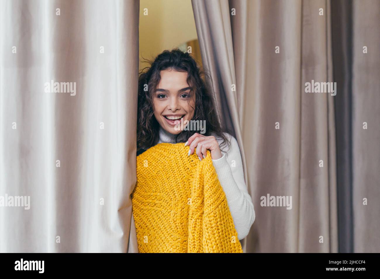 Porträt eines jungen schönen Mädchen glücklich Frau in einem Bekleidungsgeschäft in der Mall, mit einem Kleiderbügel mit einem gelben warmen Pullover, geht in die Umkleide Stockfoto