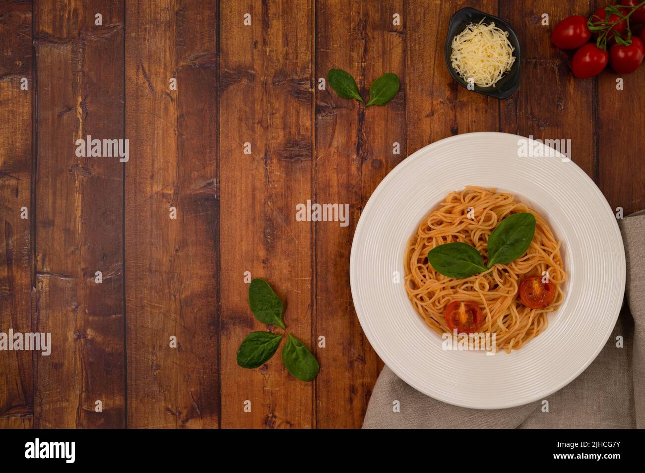 Spaghetti mit Tomatensauce, gebratenen Kirschtomaten, geriebenem Käse und Basilikumblättern auf einer braunen Tischplatte aus Holz. Draufsicht. Stockfoto