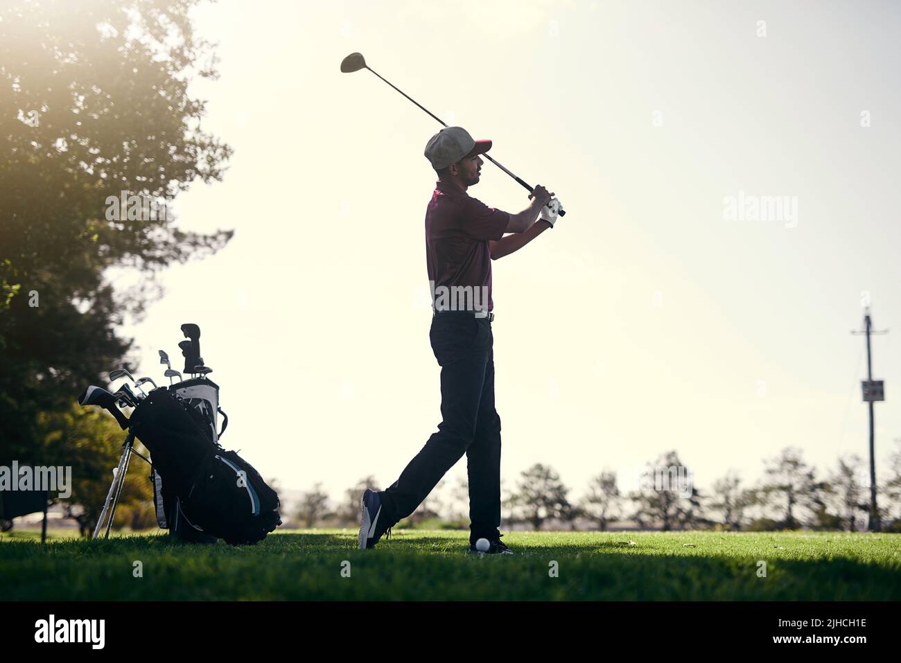 Was für ein Tag zum Golfen. Ein fokussierter junger Golfer im Begriff zu schwingen und einen Schuss mit seinem Golfclub draußen auf einem Kurs zu spielen. Stockfoto