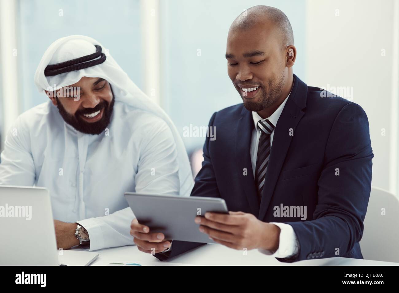 Zwei Geschäftsleute, die ein digitales Tablet und einen Laptop benutzen, während sie in einem modernen Büro eine Diskussion führen. Stockfoto