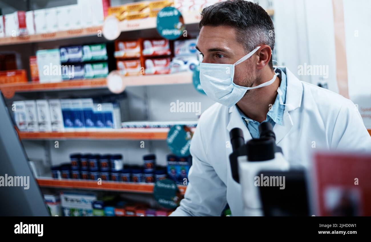 Brandneue Medikamente in der Entwicklung. Ein reifer Mann, der einen Computer benutzt, während er in einer Apotheke arbeitet. Stockfoto