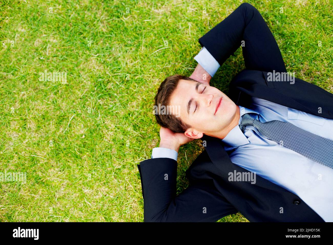Entspannter junger Geschäftsmann, der friedlich auf dem Gras schläft. Entspannter junger Unternehmer schläft friedlich auf Gras - Copyspace. Stockfoto