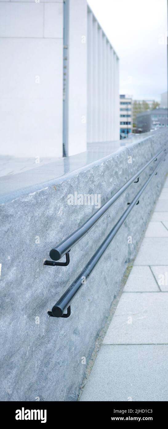 Nahaufnahme eines Metallgeländers an einer grauen Steinmauer in der Stadt. Makroansicht der Handläufe in der Innenstadt mit städtischen Gebäuden im Hintergrund. Balance und Stockfoto