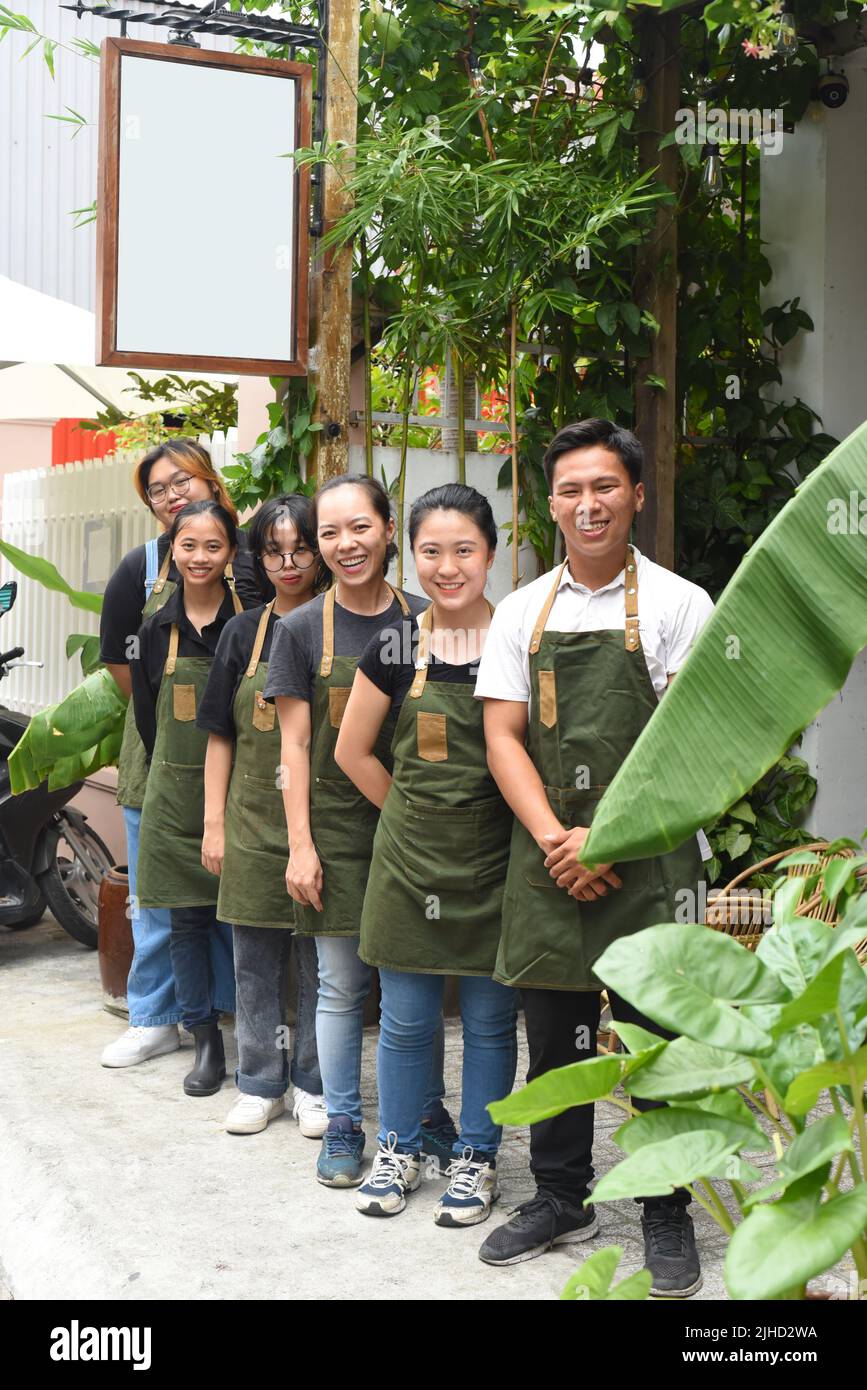 Vietnamesisches Café-Team lächelt und steht zusammen gegen ein Café Stockfoto
