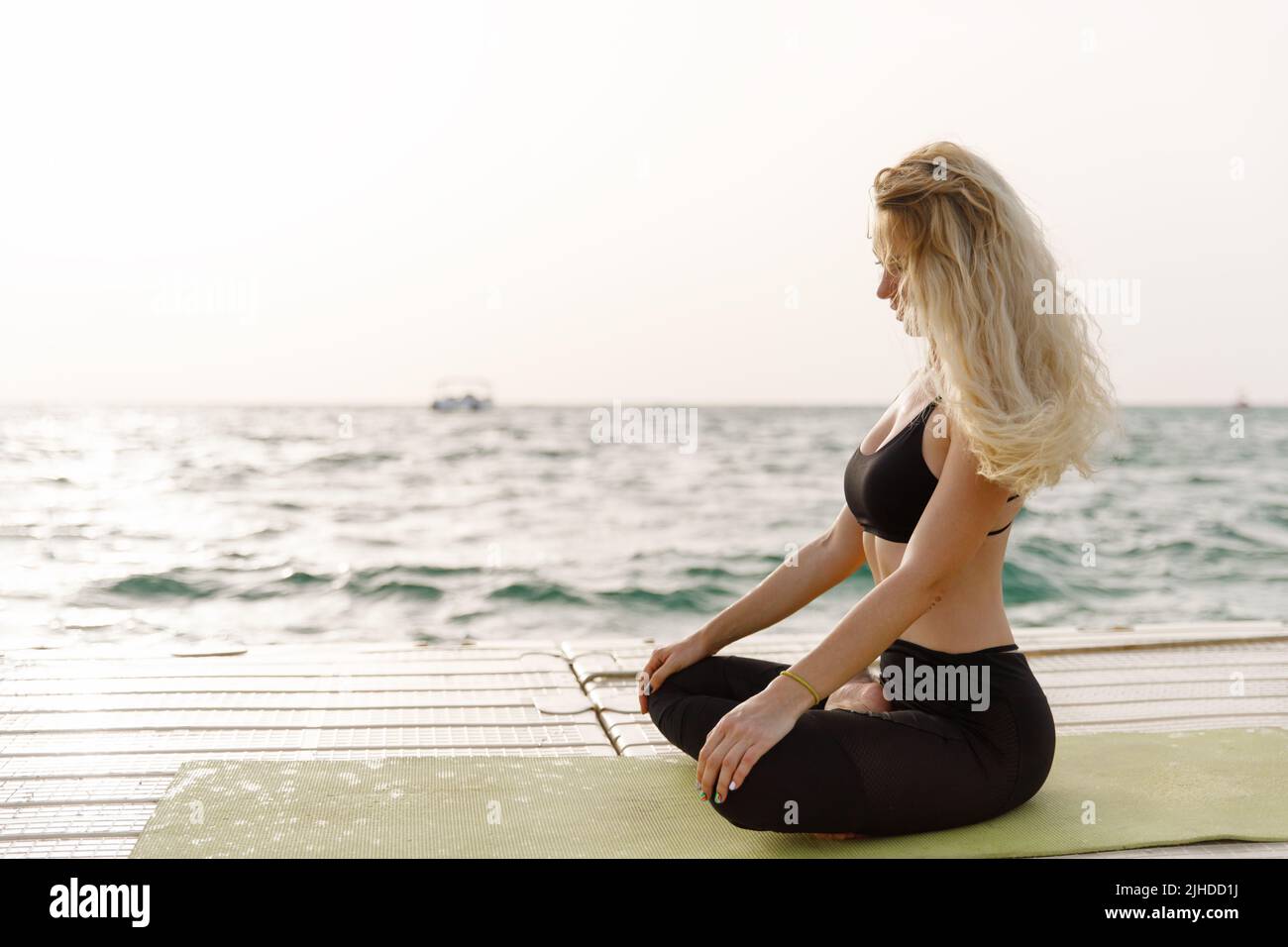 Eine junge Frau praktiziert Yoga an der Meeresküste während des Sonnenaufgangs. Stockfoto