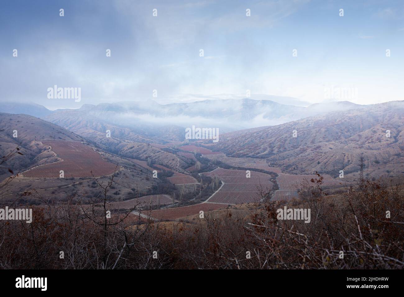 Eine gebirgige Herbstlandschaft. Weinberge in rot, Berge. Ein gemütliches Weingut im Tal. Vorderansicht. Stockfoto