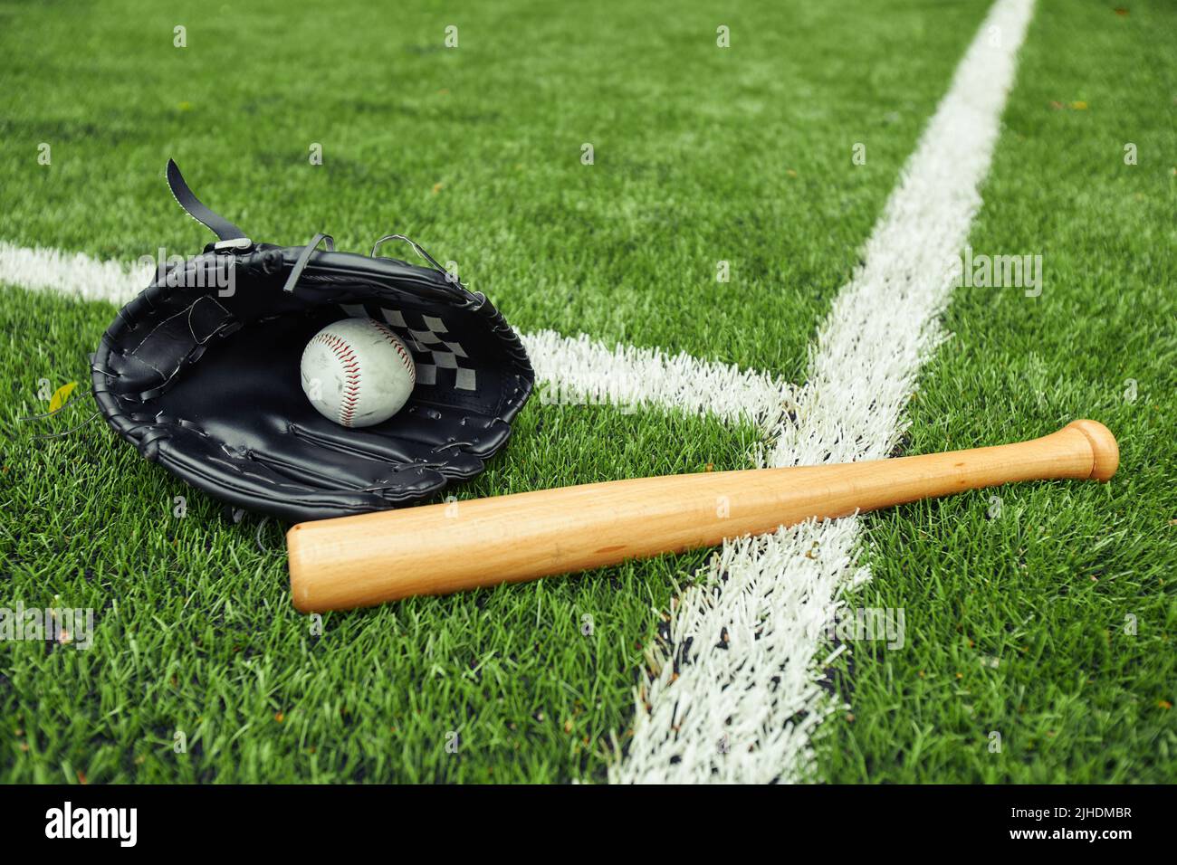 Nahaufnahme eines Baseballhandschuhs mit Ball und Schläger auf dem grünen Feld, der sich auf das Baseballspiel vorbereitet Stockfoto