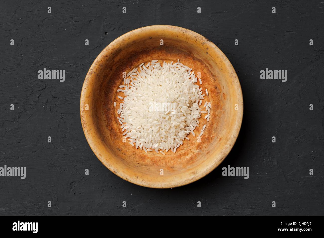 Haufen von trockenem Reis in einer Schüssel auf schwarzem Hintergrund, Mangel an Nahrung, Hunger-Konzept Stockfoto