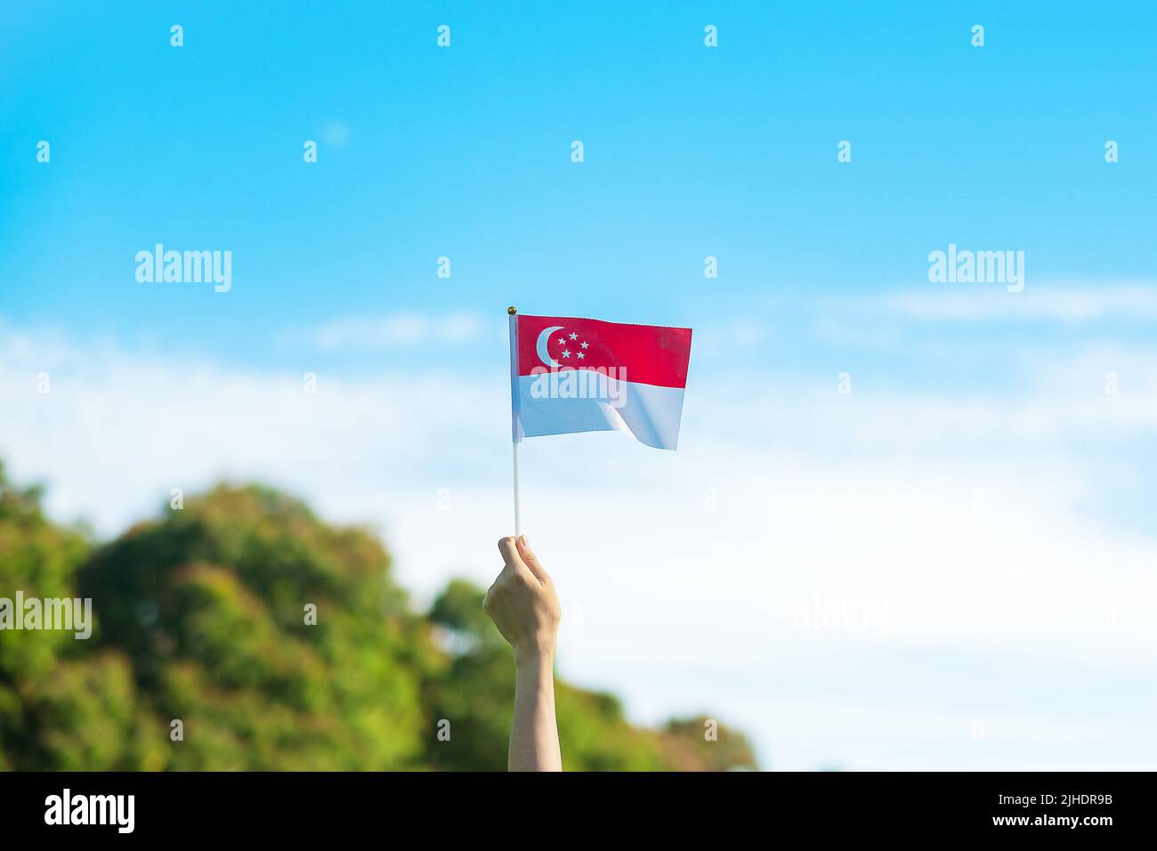 Hand mit Singapur-Flagge auf blauem Himmel Hintergrund. Singapore National Day und Happy Celebration Konzepte Stockfoto