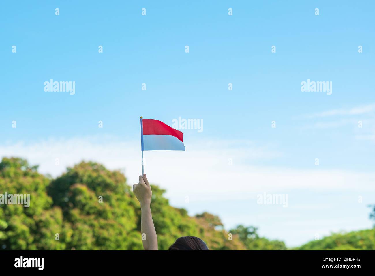 Hand hält Indonesische Flagge auf blauem Himmel Hintergrund. Indonesiens Unabhängigkeitstag, nationaler Feiertag und Happy-Party-Konzepte Stockfoto