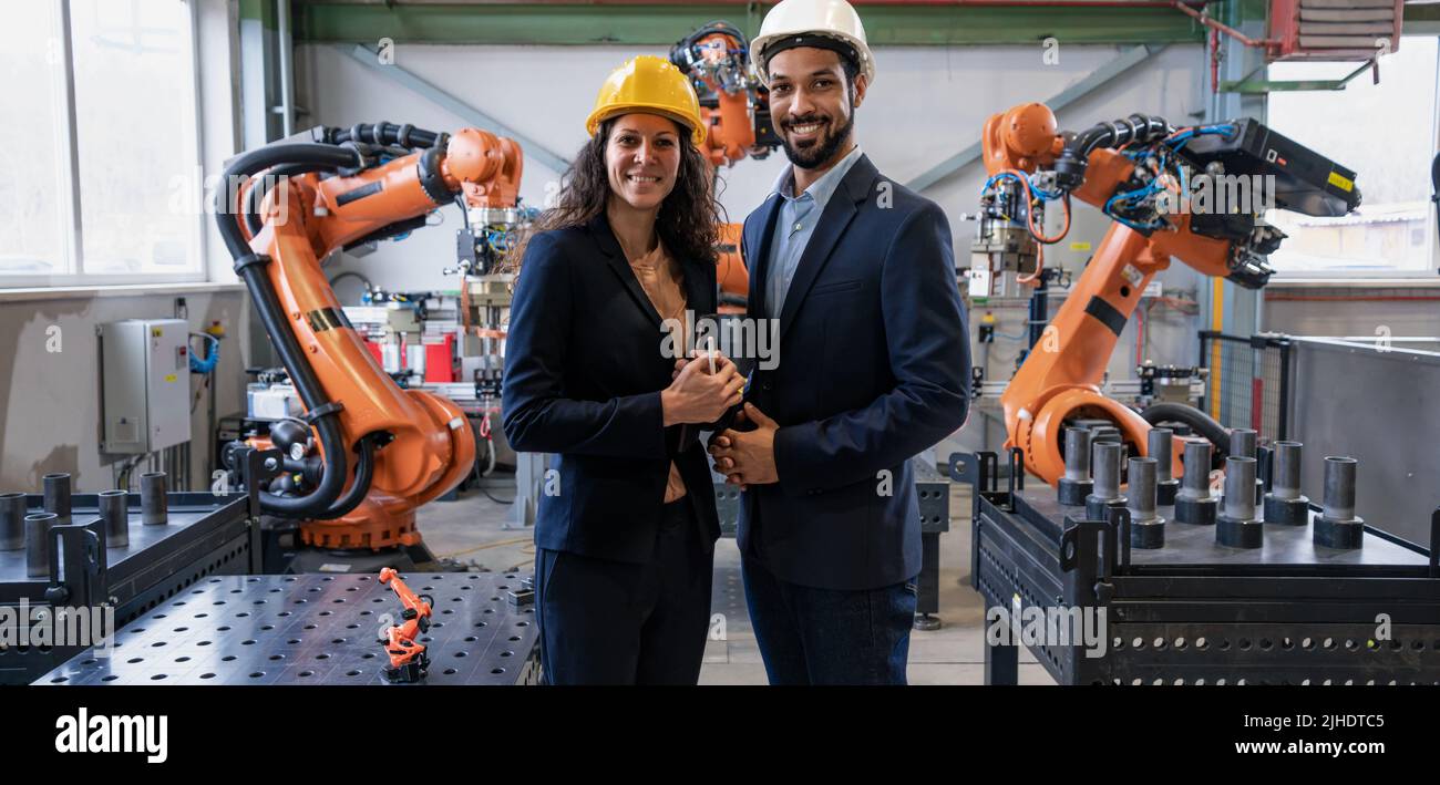 Porträt eines Ingenieurs mit seiner Kollegin, die in der Fabrik vor Roboterarmen steht. Stockfoto
