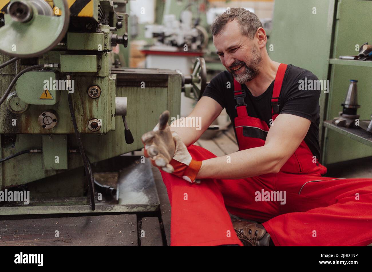 Arbeiter, der nach einem Unfall in der Fabrik unter Schmerzen leidet. Erste-Hilfe-Unterstützung beim Arbeitsplatzkonzept. Stockfoto