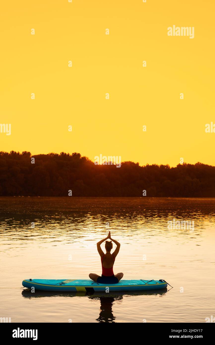Eine Frau, die Yoga auf ihrem Paddle Board macht, um sich während einer sommerlichen Hitzewelle abzukühlen Stockfoto