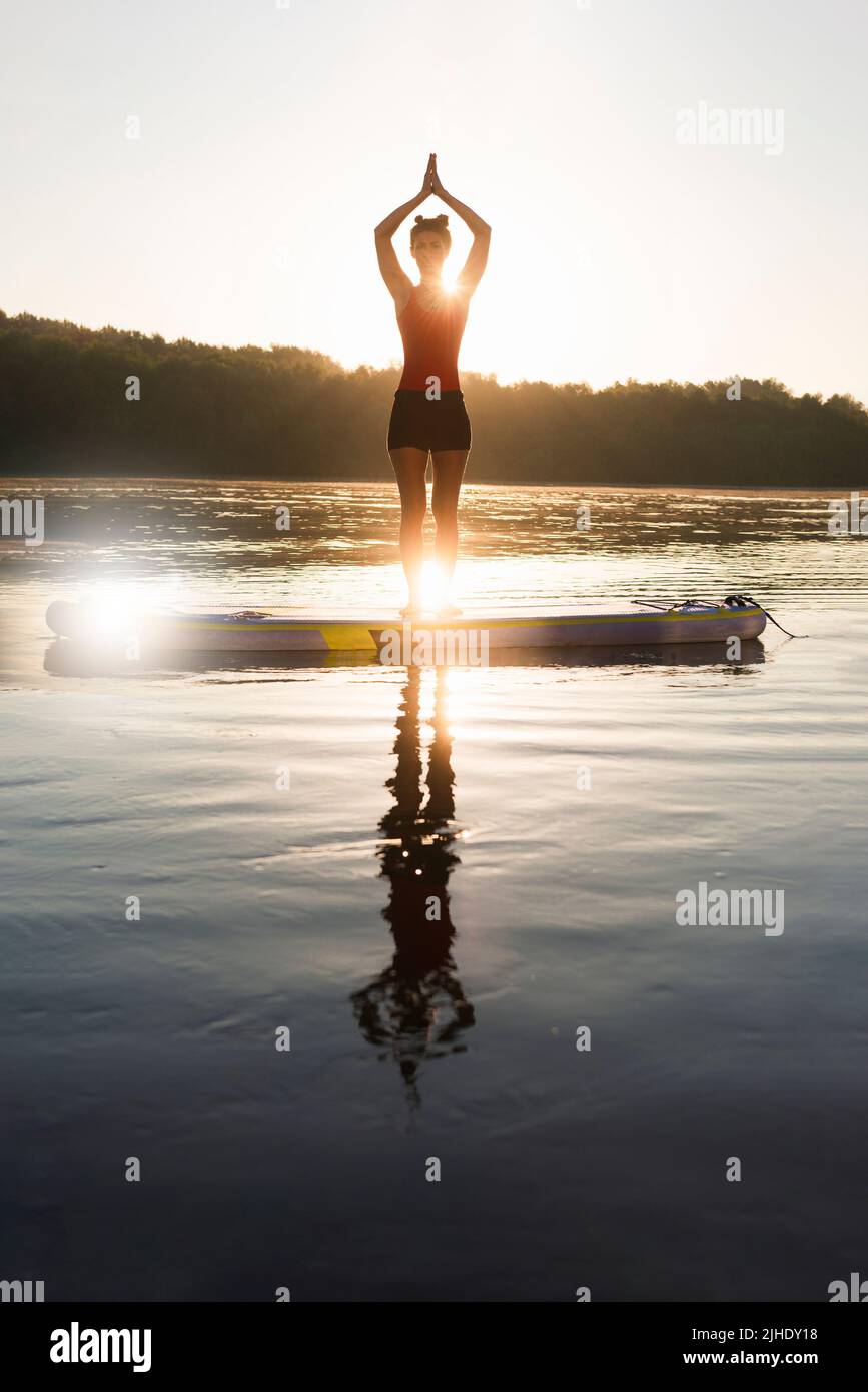 Eine Frau kühlt sich ab und praktiziert Yoga während des Sonnenaufgangs. Stockfoto