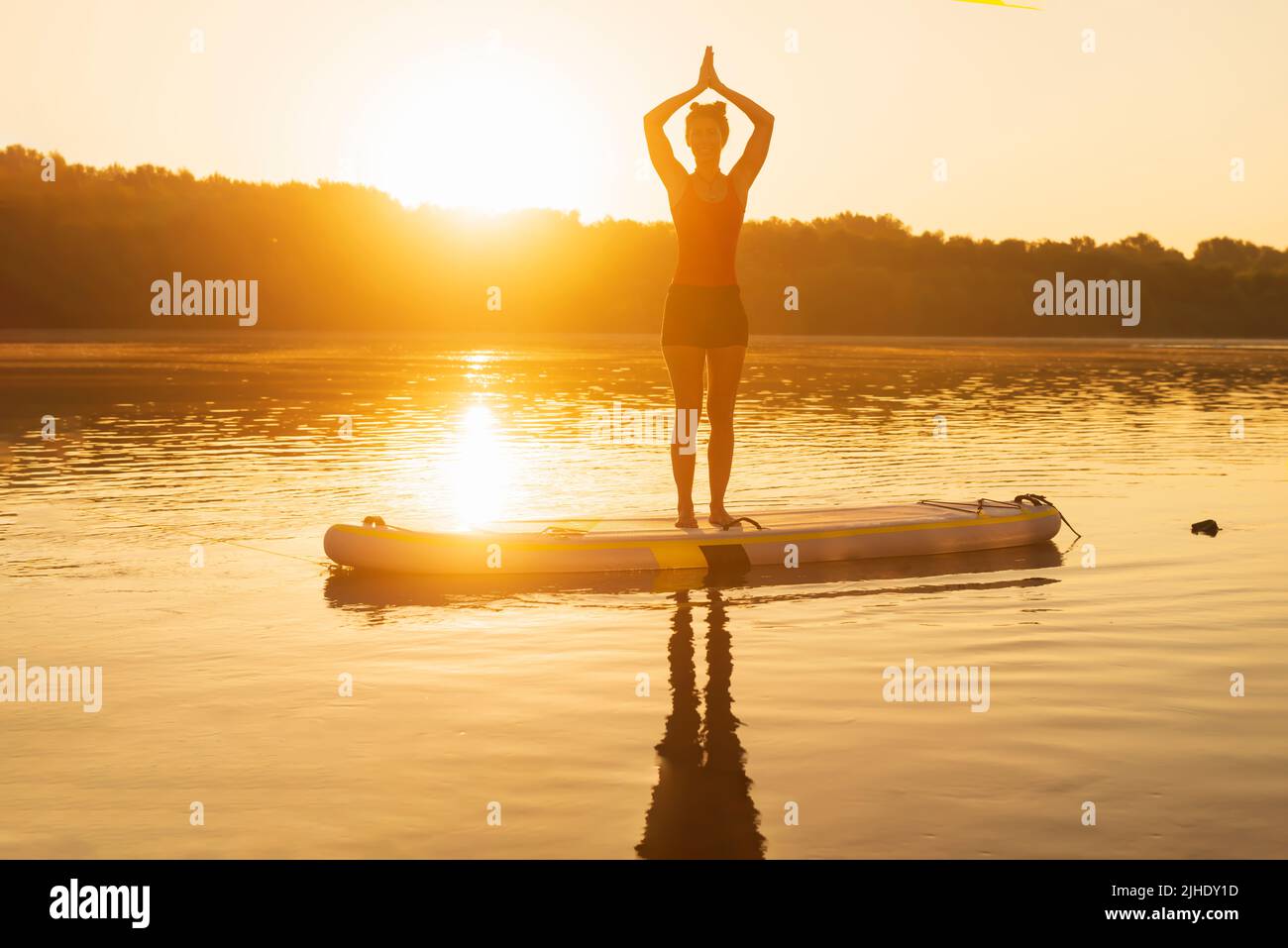 Eine Frau kühlt sich an einem heißen Sommertag durch Yoga auf dem Paddle Board ab. Stockfoto