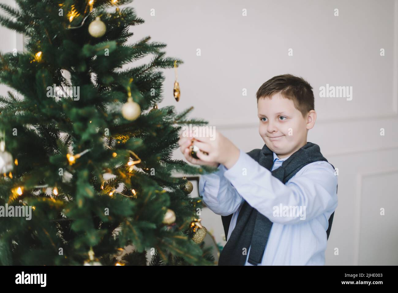 Lächelnder kaukasischer Junge, der Weihnachtsbaum in einer häuslichen Inneneinrichtung und festlicher Atmosphäre schmückt Stockfoto