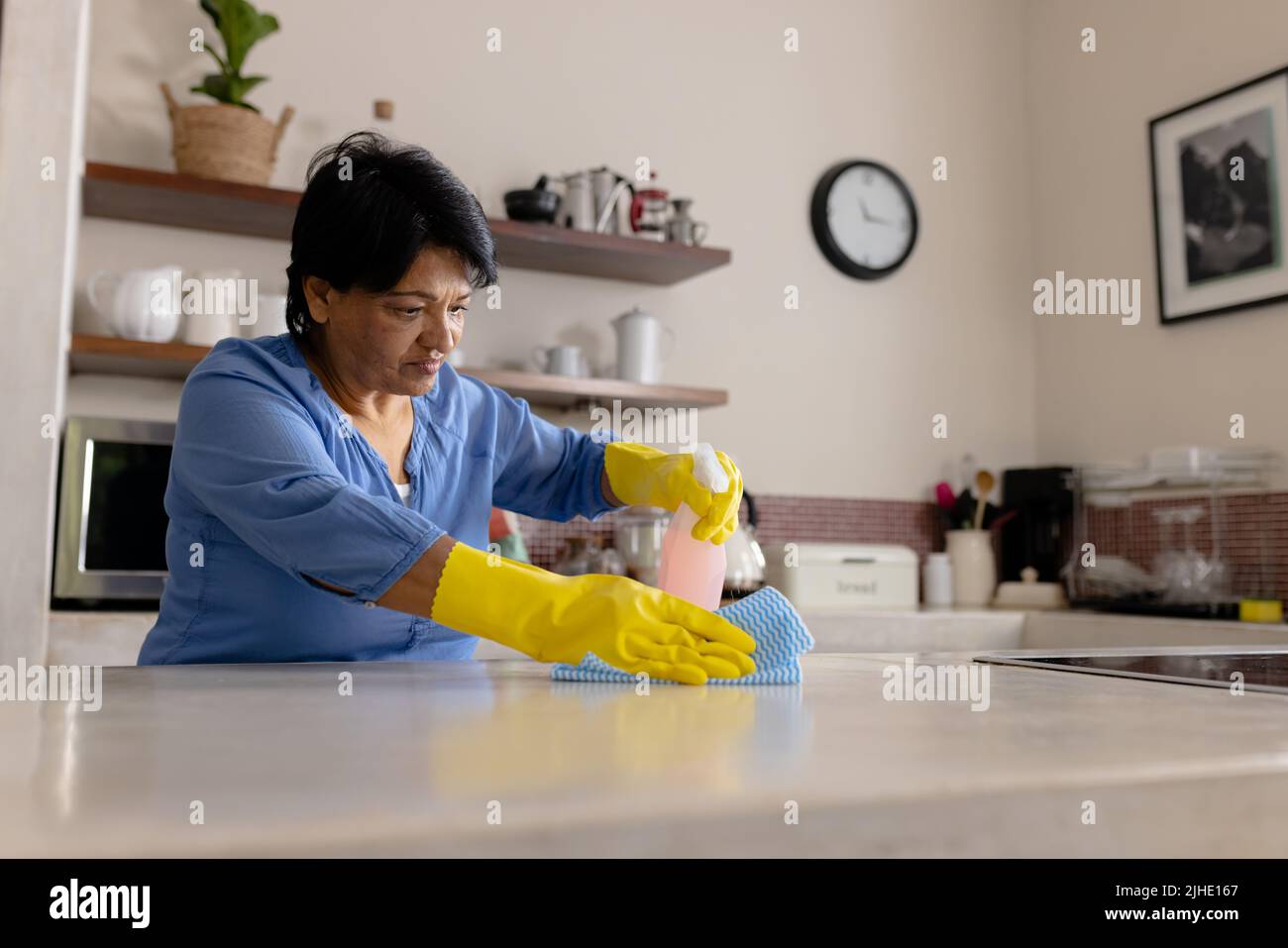 Biracial reife Frau trägt Handschuhe Reinigung Kücheninsel mit Lappen und Sprühflasche, kopieren Raum Stockfoto