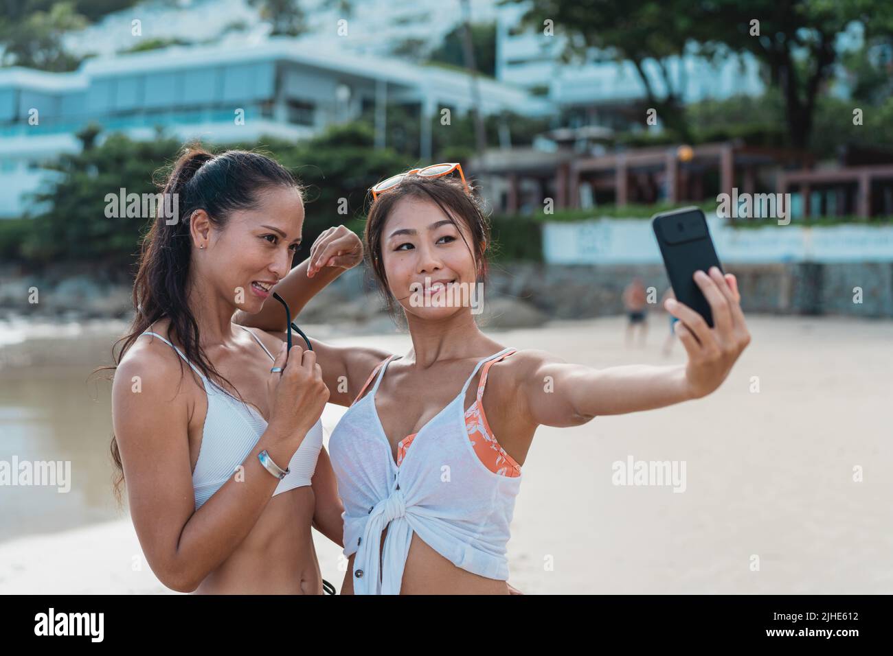 Portrait von glücklichen lächelnden schönen Frauen, die ein Selfie-Foto mit dem Handy am Strand machen. Hübsche junge asiatische Mädchen in Bademode posiert und für Bild zusammen auf tropischen Urlaub Stockfoto
