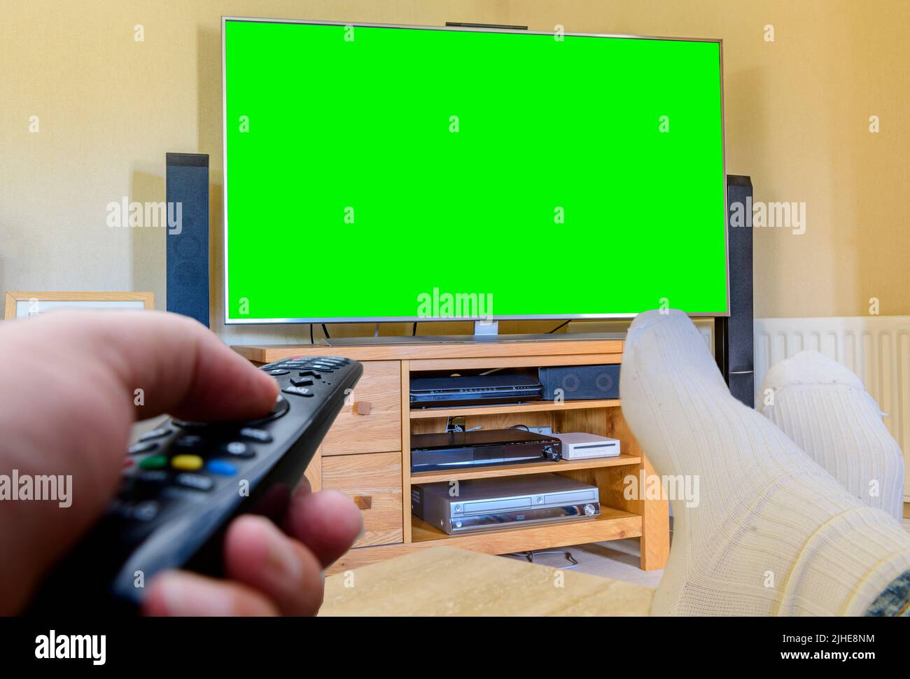 Couch Potato man mit den Füßen nach oben und einem großen, grünen Flachbildfernseher mit Fernbedienung, der die Sender in der Hand wechselt Stockfoto