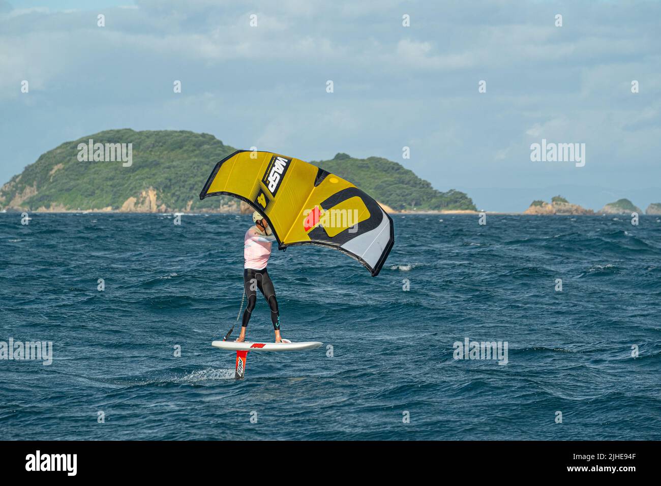 Ein Mann Flügel Folien auf dem Meer mit einem Hand gehalten aufblasbaren Flügel, Reiten ein Tragflächenboot Surfboard Flügel Folie Bord. Hauraki Gulf, Auckland, Neuseeland. Stockfoto