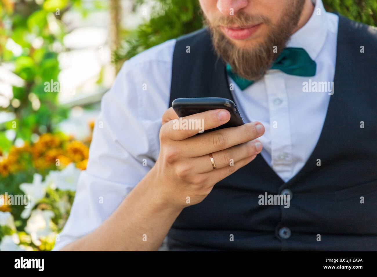 Nahaufnahme auf einem Smartphone in der Hand eines bärtigen Hipsters in einem Anzug, Sommer im Freien Stockfoto