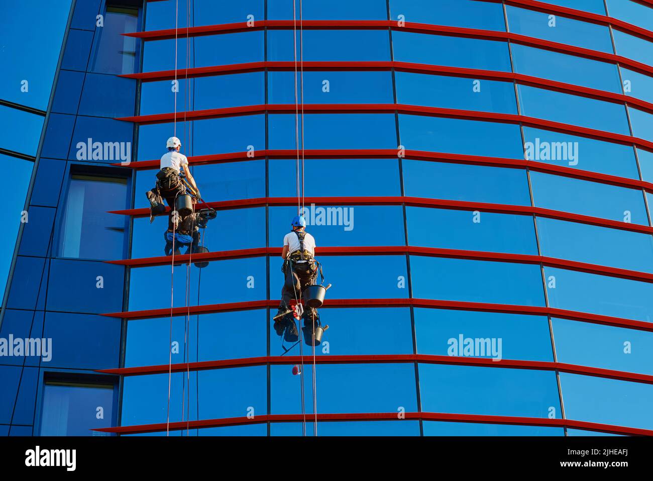 Zwei Arbeiter putzen Fenster im Business Center, Industrielle Alpinisten waschen außen des Wolkenkratzers, gefährliche riskante Arbeit in der Höhe, Reinigungsservice Stockfoto