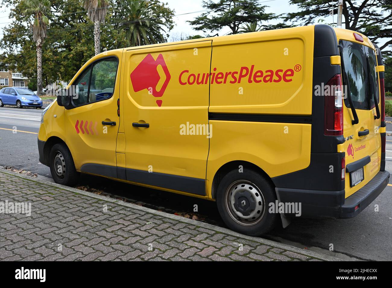 Seitenansicht eines gelben Couriers Please van, eines Renault-Verkehrs, der neben einem Fußweg geparkt ist, mit markanten Firmenlogos Stockfoto