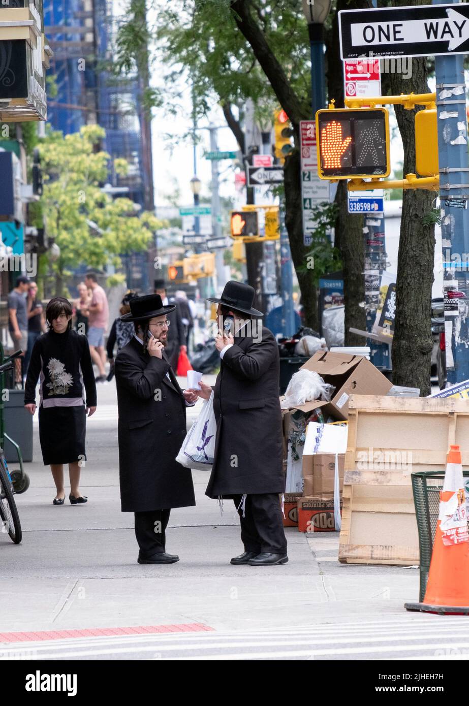 Zwei chassidische jüdische Männer scheinen gleichzeitig miteinander zu sprechen und auch ihre Handys zu benutzen. An der Lee Avenue in Brooklyn, New York. Stockfoto