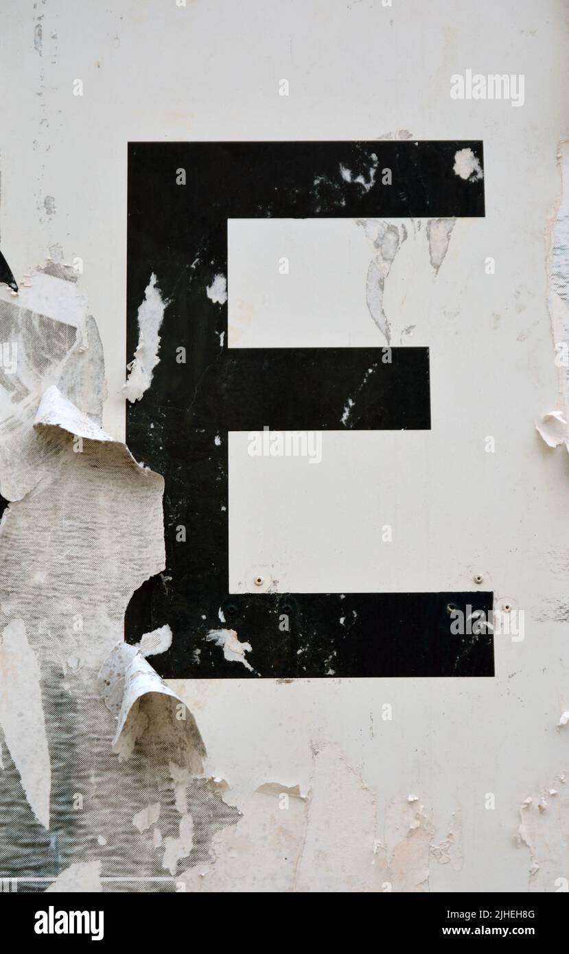 Der Buchstabe E in Schwarz auf einer zerrissenen und verwitterten Plakatwand Stockfoto