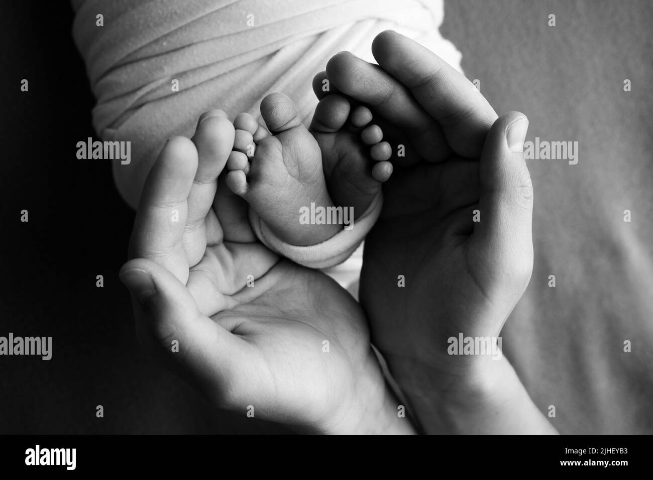 Ein Vater und eine Mutter halten ein neugeborenes Baby an den Beinen. Foto von Fuß, Fersen und Fingern. Schwarzweiß-Makrofotografie Stockfoto