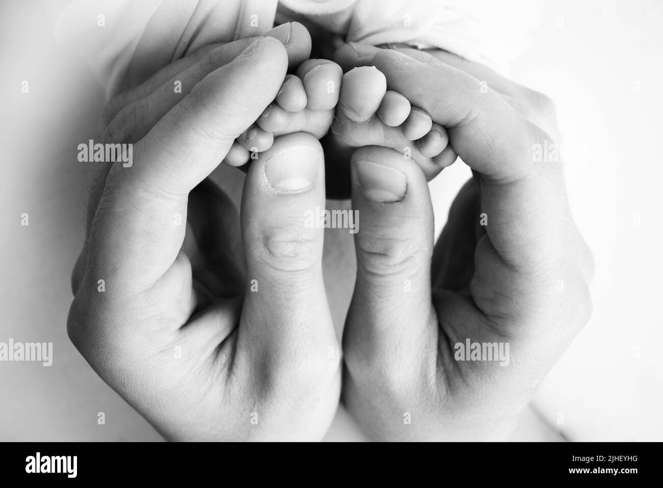Ein Vater und eine Mutter halten ein neugeborenes Baby an den Beinen. Foto von Fuß, Fersen und Fingern. Schwarzweiß-Makrofotografie Stockfoto