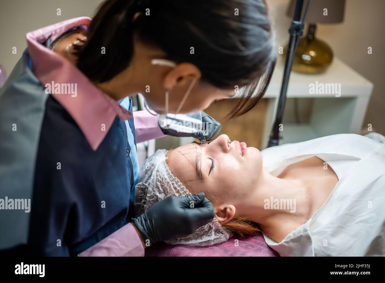 Der Meister des Permanent Make-up-Kosmetologen nimmt Messungen für die neue Form der Augenbrauen des Modells vor. Vorbereitung der Mikrobladenbehandlung Stockfoto